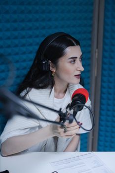 Portrait of a woman recording in a soundproof studio, wearing headphones and speaking into a microphone.