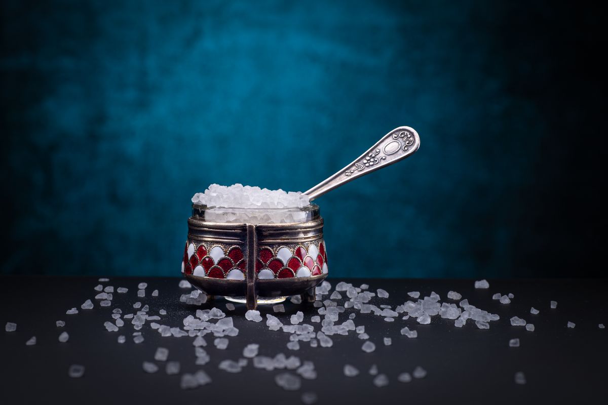 Close-up of a vintage sugar bowl with spoon on dark background, showcasing crystals.