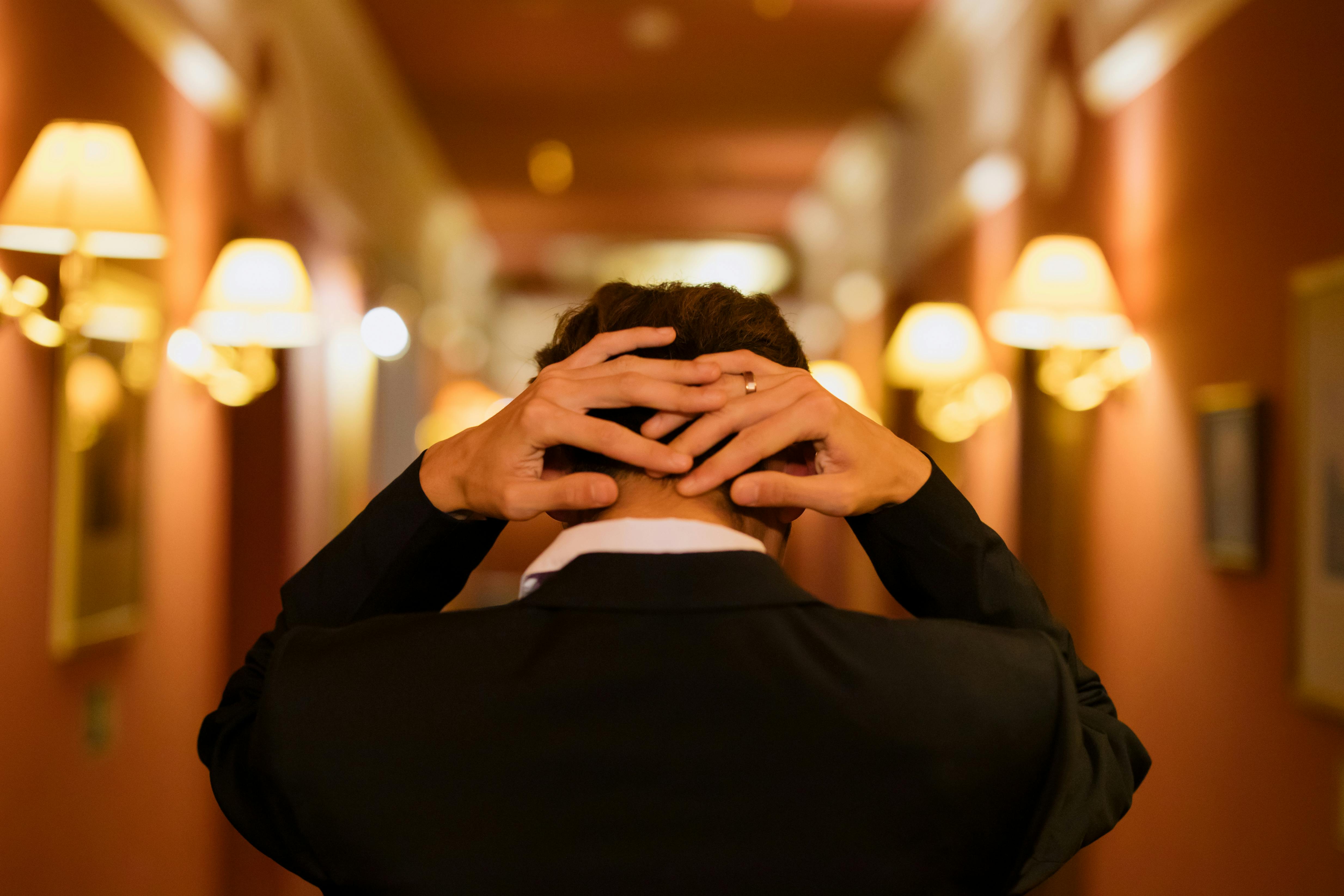 man in black suit jacket with hands on his head