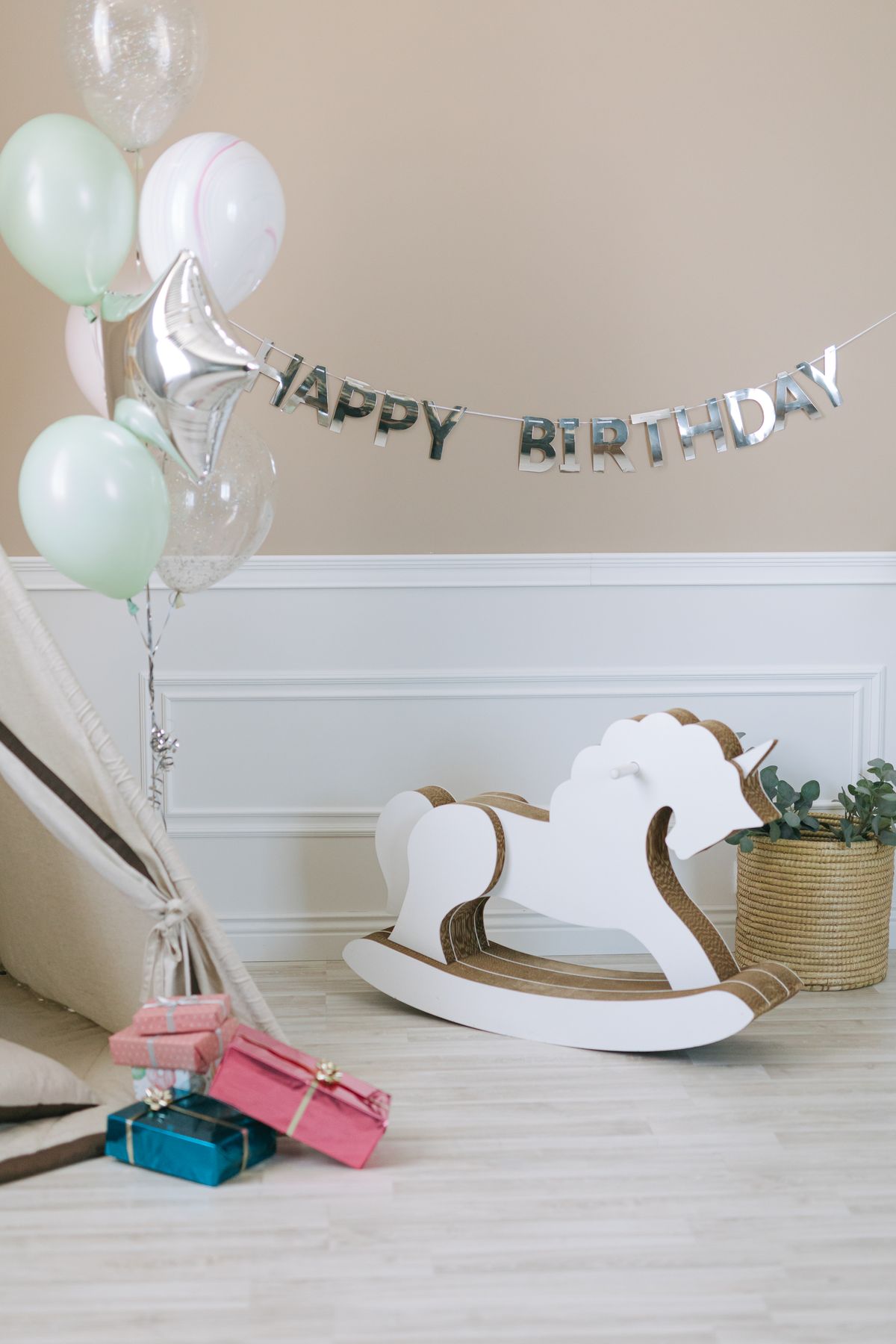 A celebration setup with balloons, gifts, and a rocking horse indoors