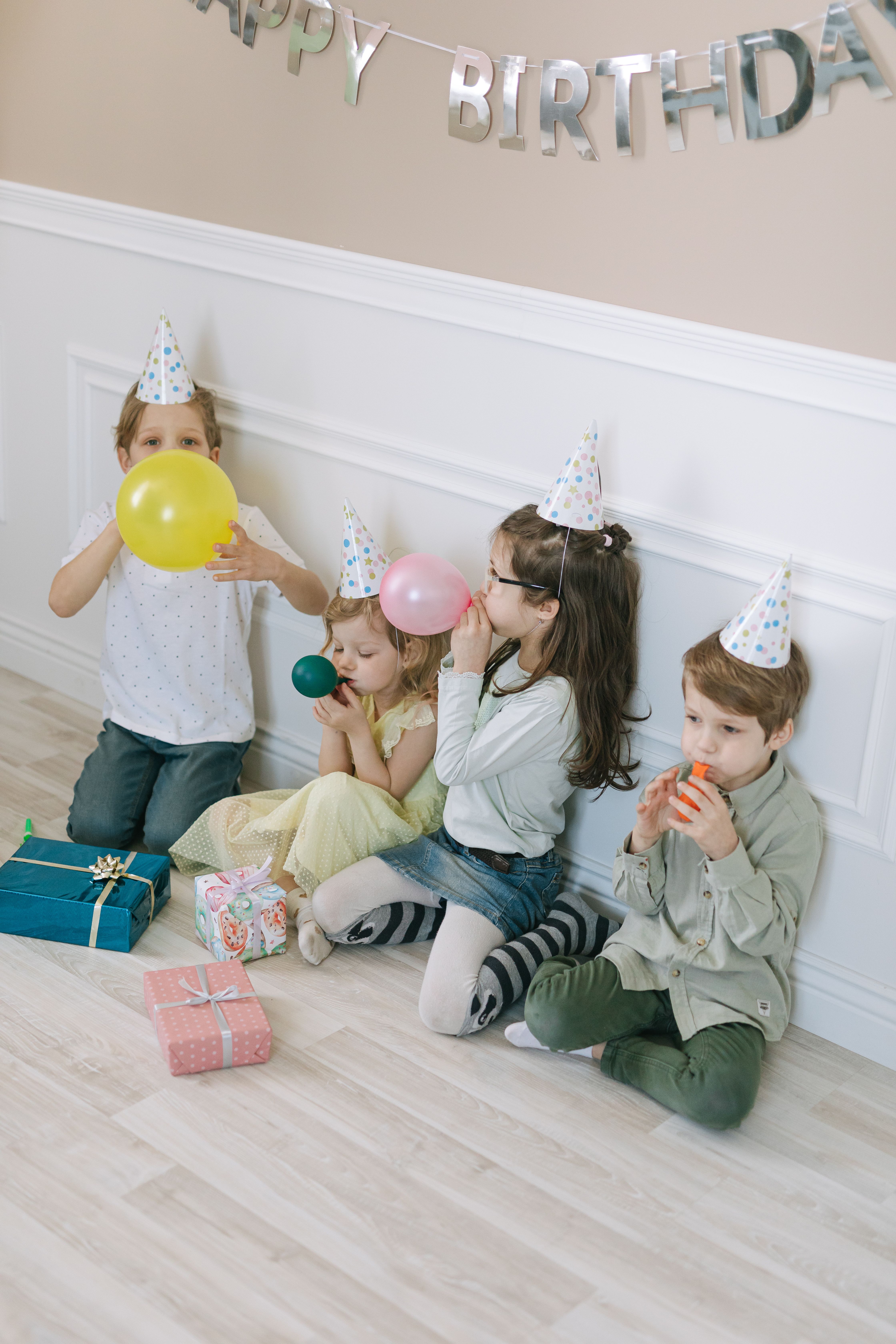 A Group of Children with Party Hats Sitting on the Floor Blowing ...