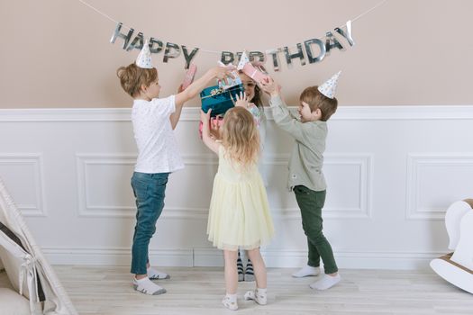 Joyful children celebrate a birthday, exchanging gifts indoors.
