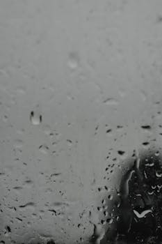 A close-up view of raindrops on a window creating a gloomy and wet atmosphere.