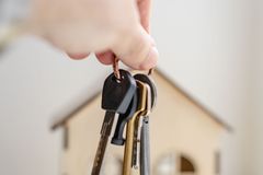 Crop faceless real estate agent with keys from new house bought with mortgage against wooden model of building