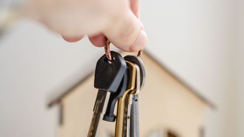 Crop faceless real estate agent with keys from new house bought with mortgage against wooden model of building