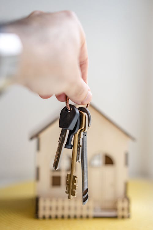 A person holding a set of keys above a miniature house model.