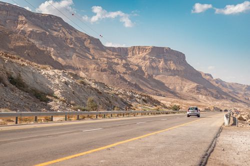 Free Narrow asphalt road running along dry rocky terrain with car under cloudy blue sky in sunny day Stock Photo