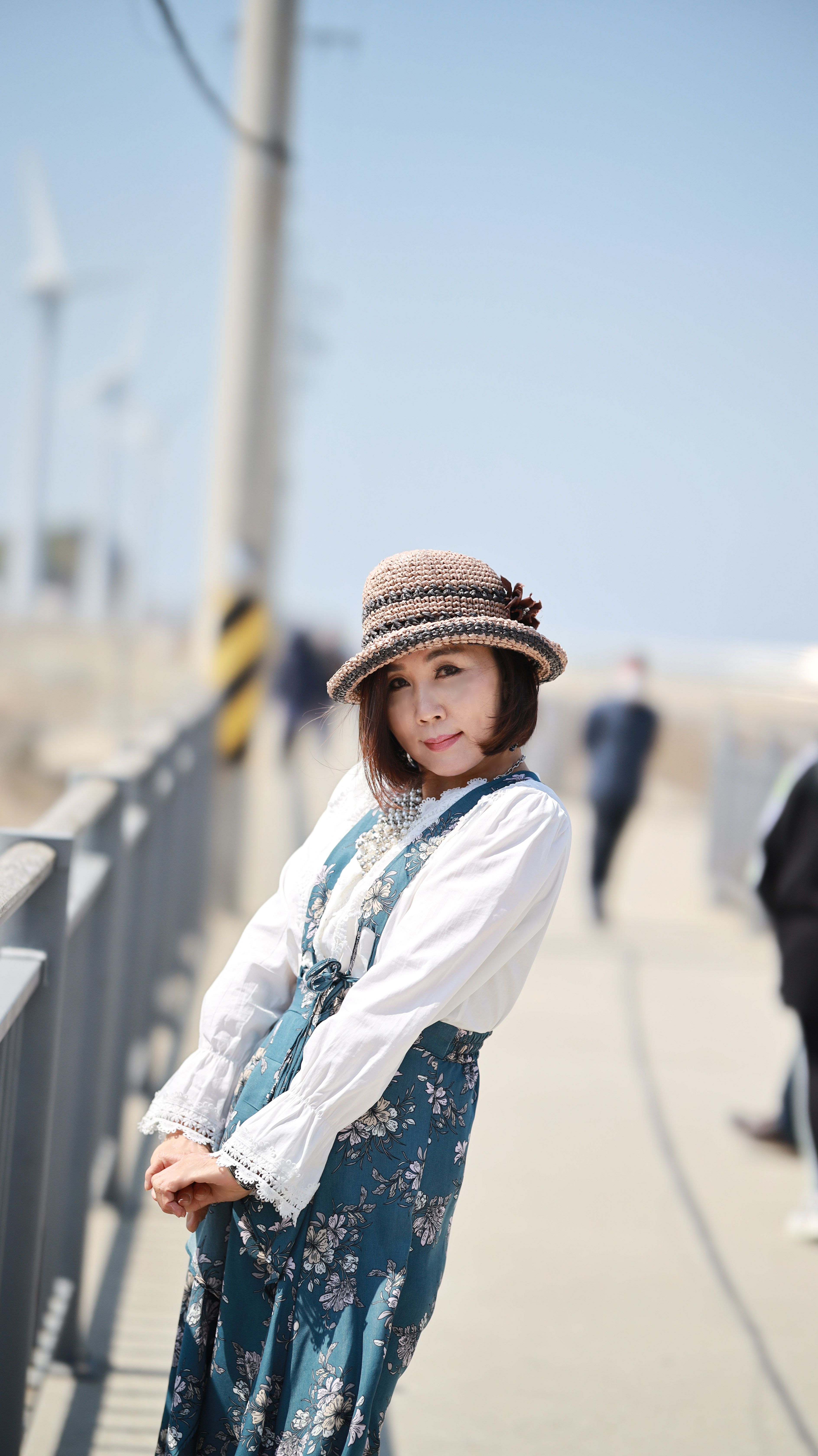 Charming woman in a floral dress and sun hat enjoying a sunny stroll on an urban walkway. Bright and cheerful portrait.