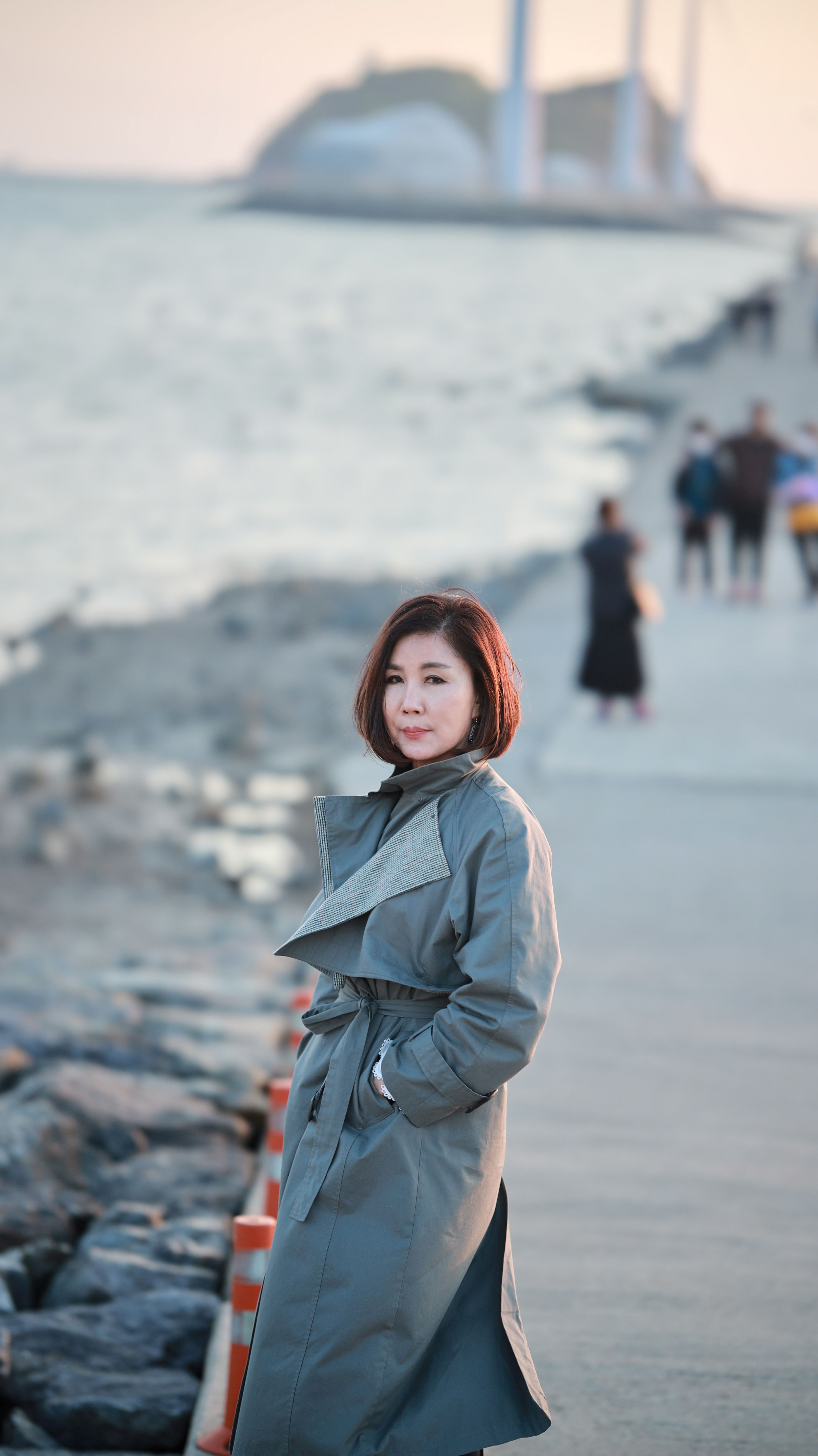 Asian woman in a coat standing by the sea during sunset.