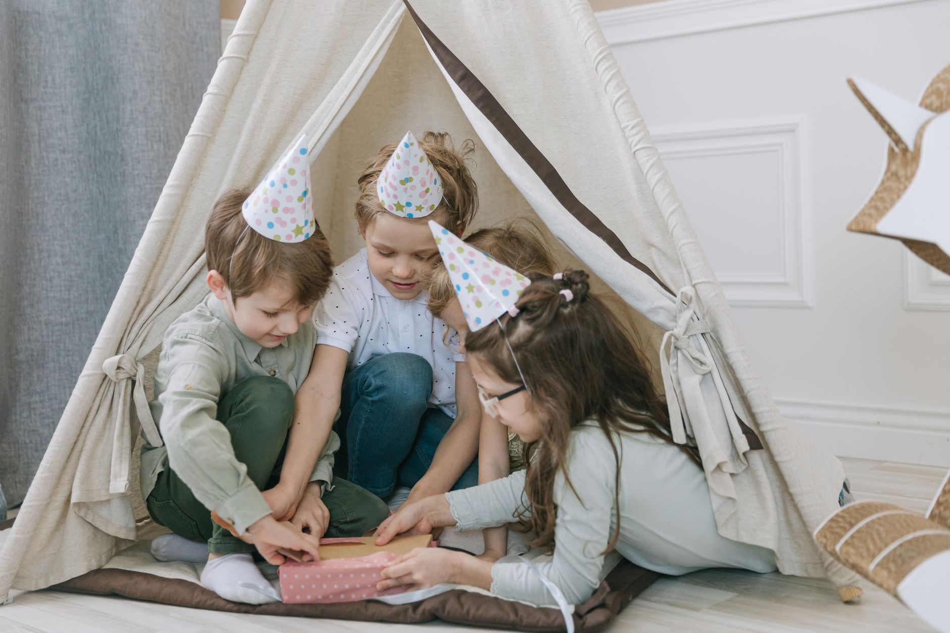 teen birthday party venues egypt — Kids wearing party hats open a gift inside a teepee, celebrating a birthday indoors.
