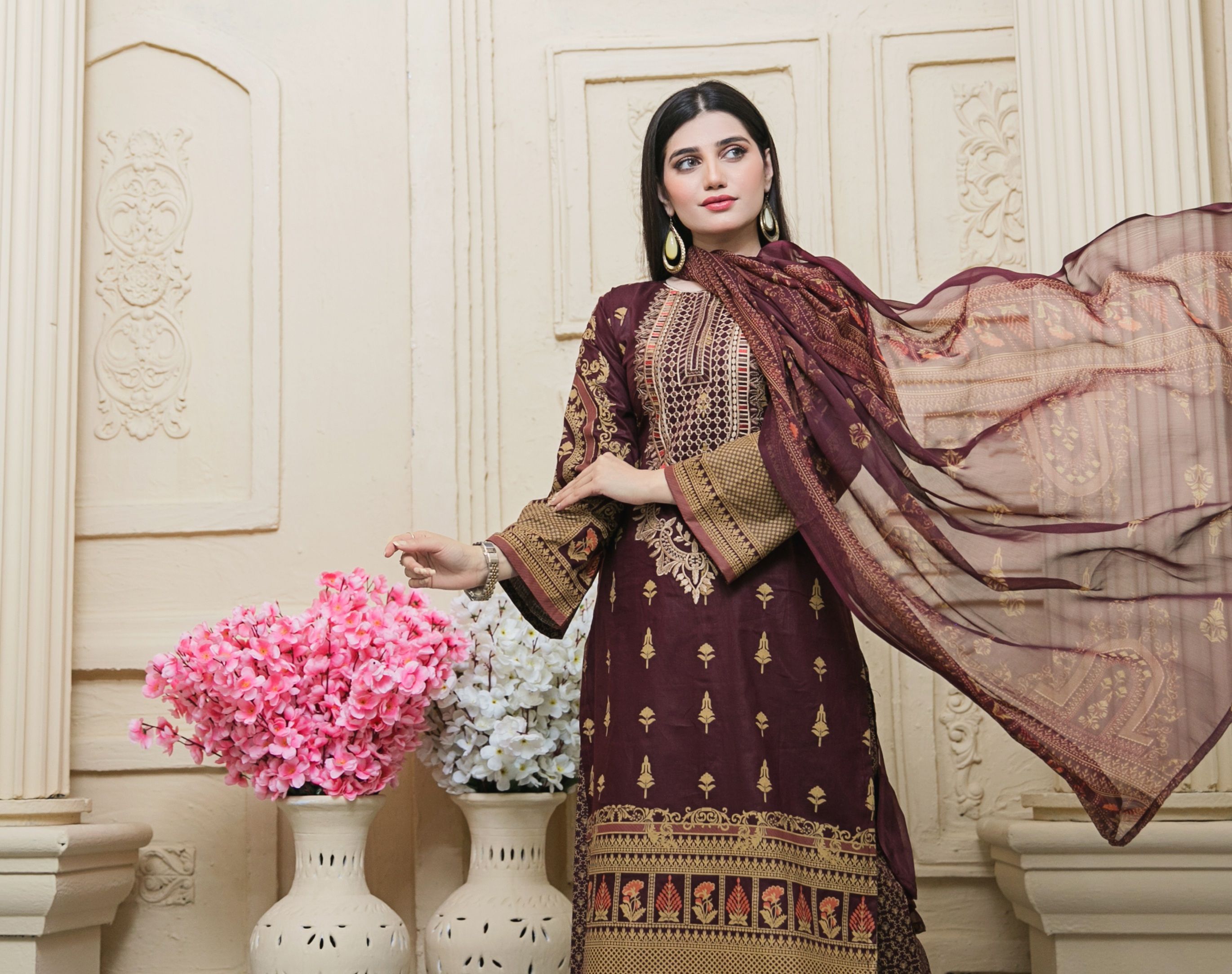 A stylish woman in traditional attire posing indoors, accented by vibrant floral decor.