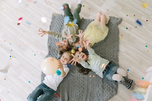 Free Aerial view of happy children celebrating with balloons and confetti indoors on a rug. Stock Photo