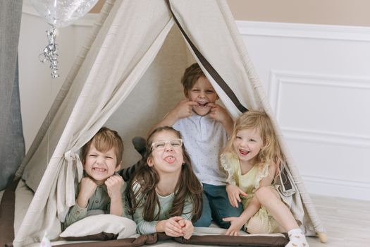 Four cheerful kids making faces inside a cozy indoor play tent, smiling and having fun.