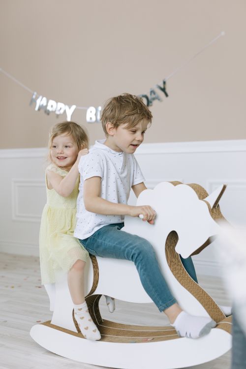 Free Two children having fun on a wooden rocking horse at a birthday celebration indoors. Stock Photo