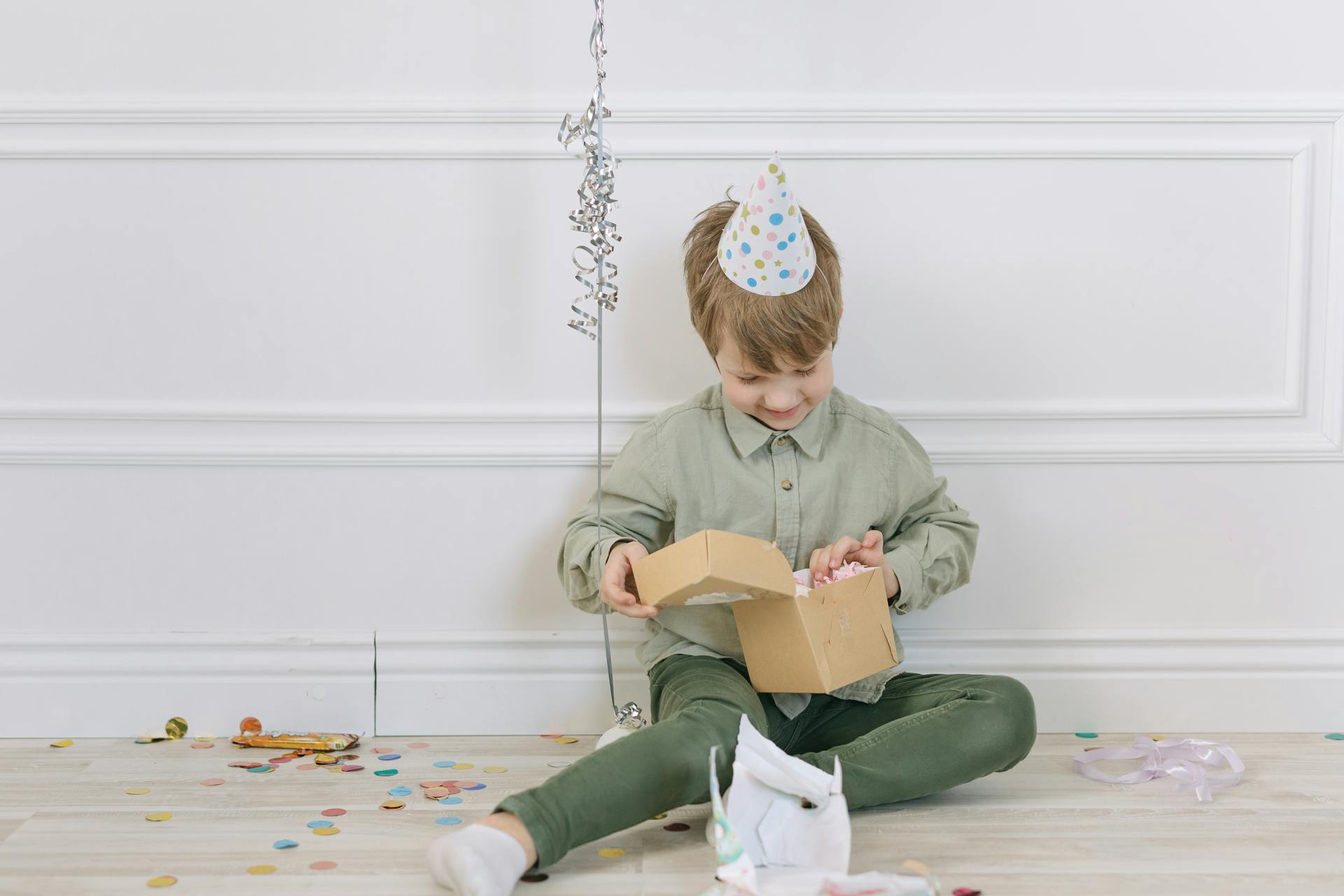 A child joyfully opens a gift box while wearing a party hat during a birthday celebration.