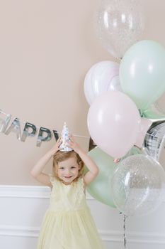 Smiling child enjoying a birthday party with balloons and party hat indoors.