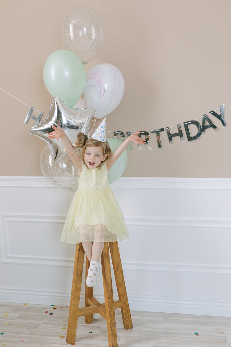 Child Wearing Party Hat Sitting On A Stool