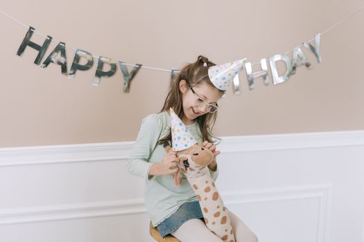 A cheerful child wearing birthday hats indoors celebrating with a stuffed animal.