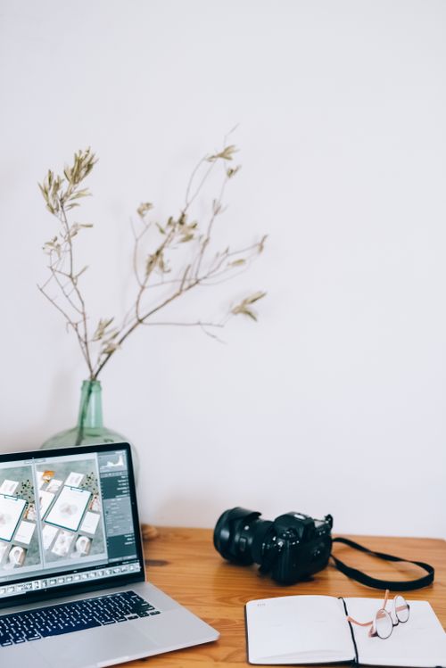 Free Minimalist desk setup featuring a camera, laptop, and decorative branches for a creative workspace. Stock Photo