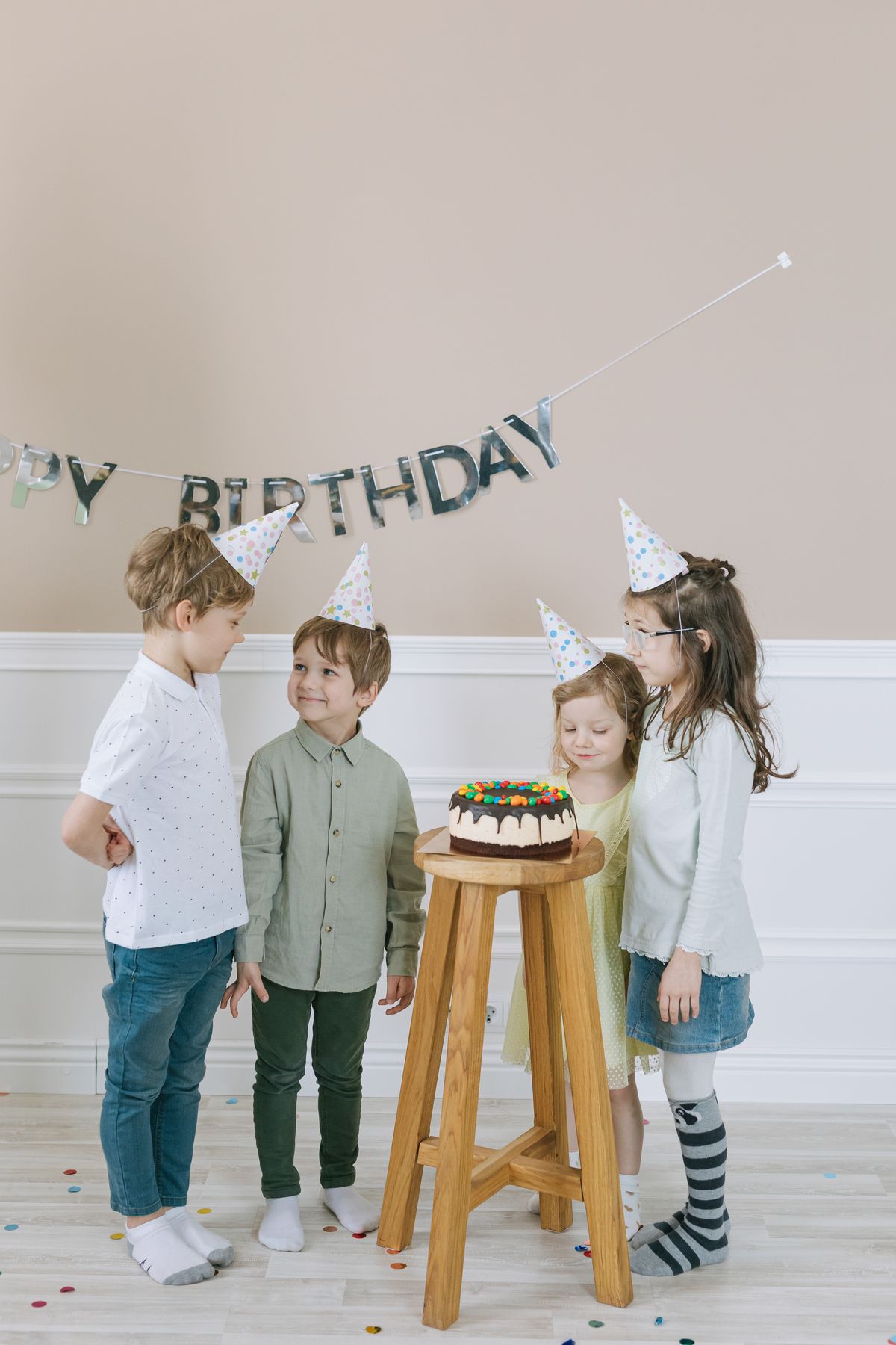 Group of kids celebrating birthday with cake and party hats, indoors. Stock Photo.