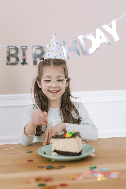 A Girl Wearing Birthday Hat Looking at the Plate with Piece of Cake