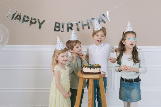A group of children celebrating a birthday with cake and balloons indoors.