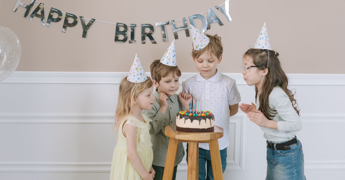 Group of children celebrating a birthday with cake and decorations indoors.