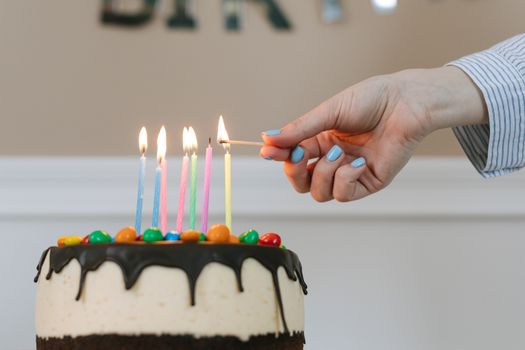 Colorful candles being lit on a delicious birthday cake indoors.
