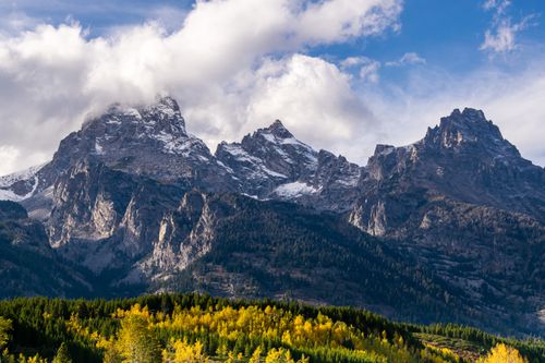 Free Scenic view of rugged alpine mountains with lush autumn forest under a cloudy sky. Stock Photo