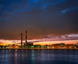 日落时分，工业烟囱在水面倒映出城市景观，展现了城市灯光与云层