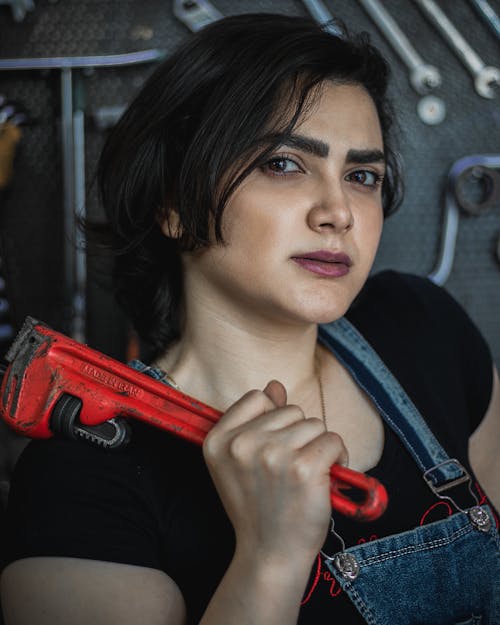 A Woman in Black Shirt and Denim Jumper Holding a Power Tool