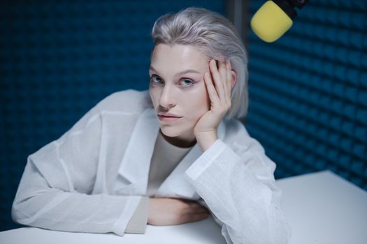 Stylish woman recording podcast in soundproof studio with microphone.