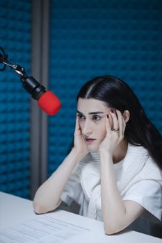 Woman at a recording studio in deep thought with a red microphone. Ideal for podcasts and audio production themes.
