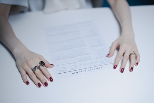 Close-up of hands with rings holding a podcast planner on a white table.