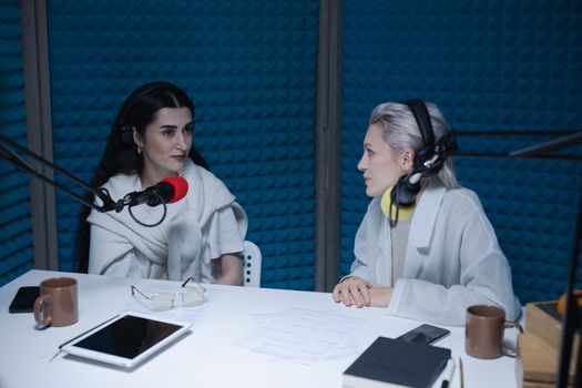 Two women engaged in a podcast recording session in a soundproof studio.