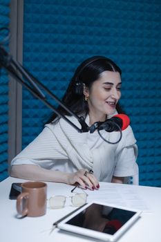 Smiling woman podcaster recording in a soundproof studio with headphones and microphone.