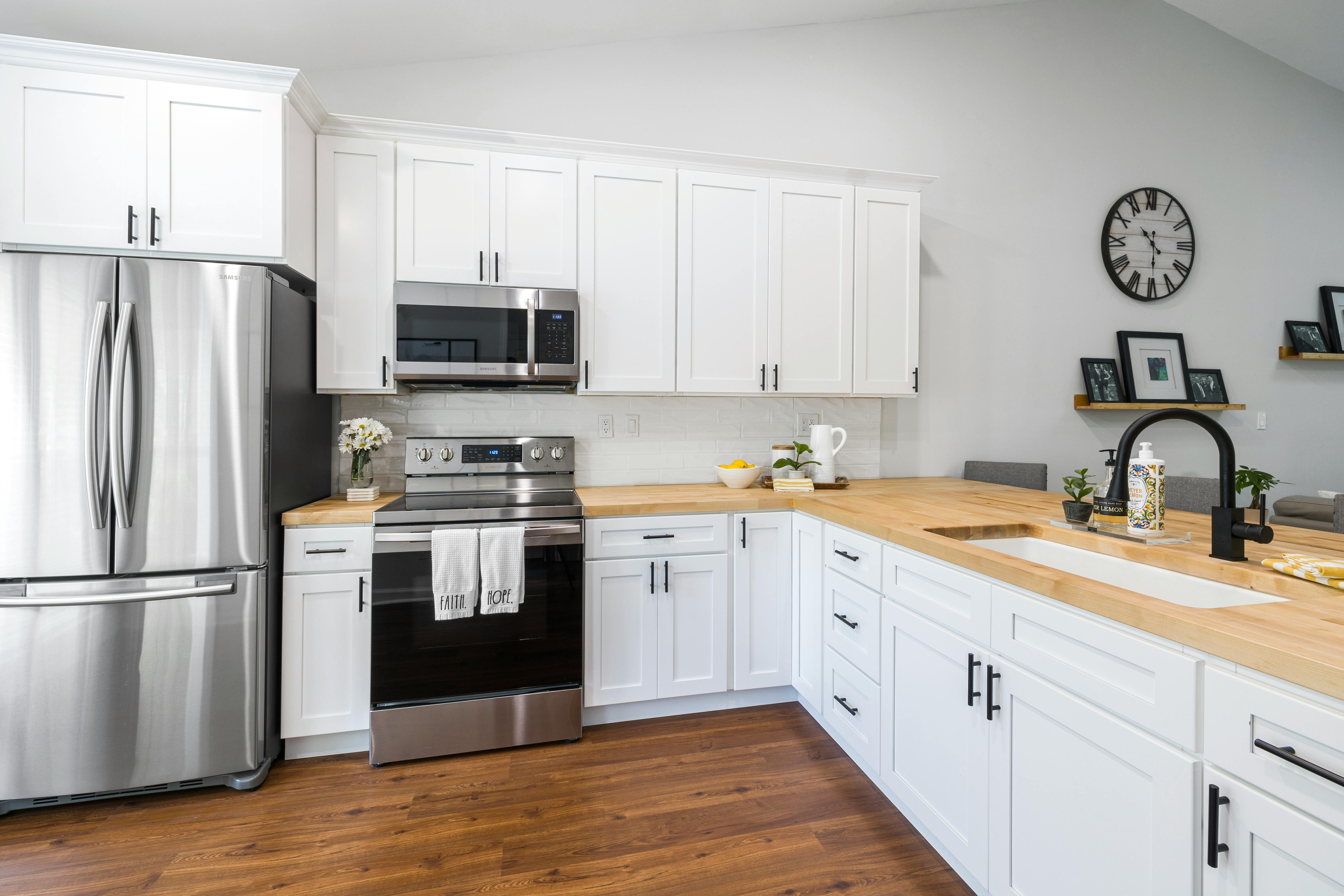 A small kitchen with stainless steel appliances, white cabinets, and a  natural light colored wood counter top Stock Photo - Alamy