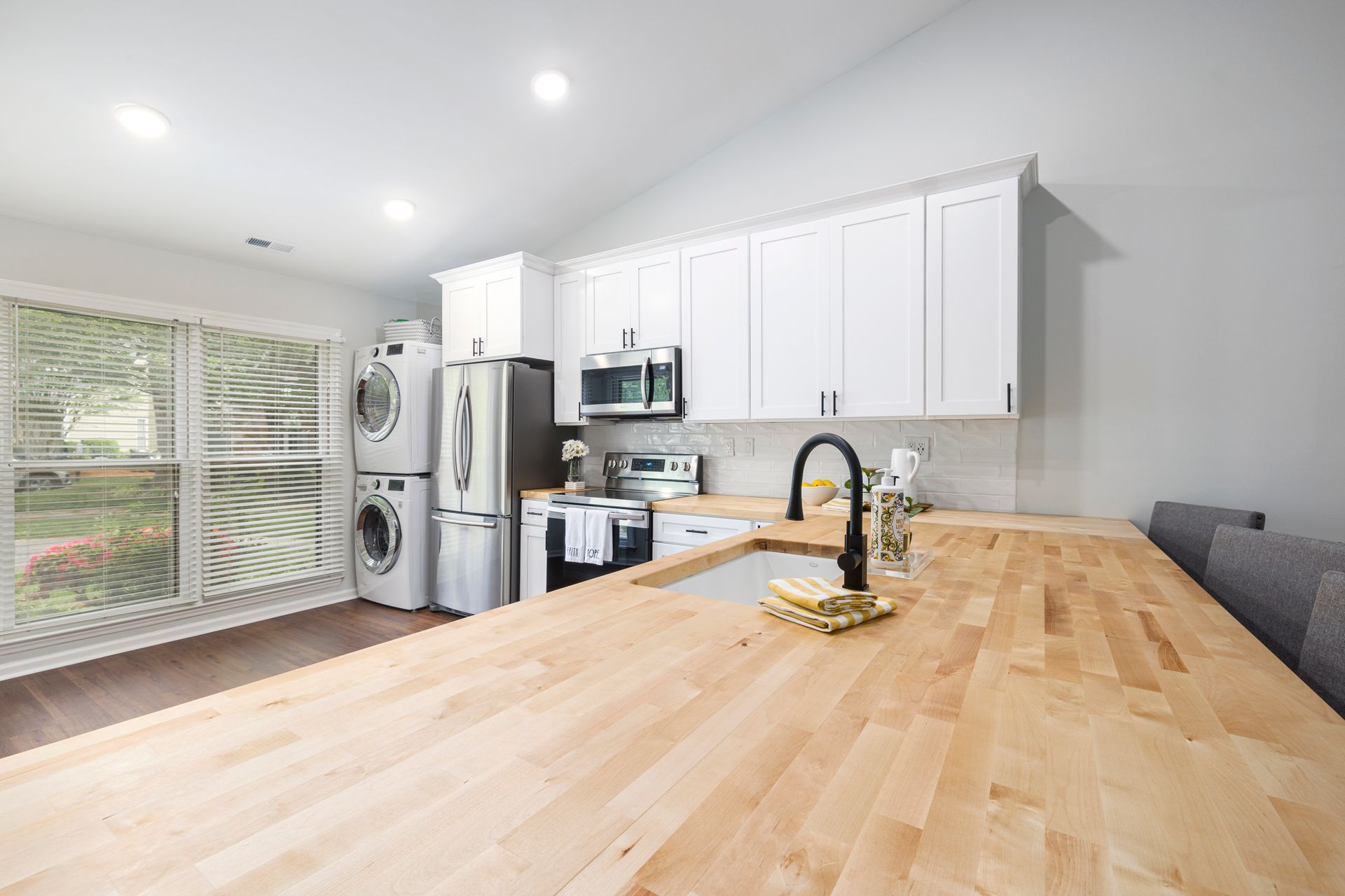 Bright modern kitchen with white cabinets, wooden countertop, and laundry appliances in view.