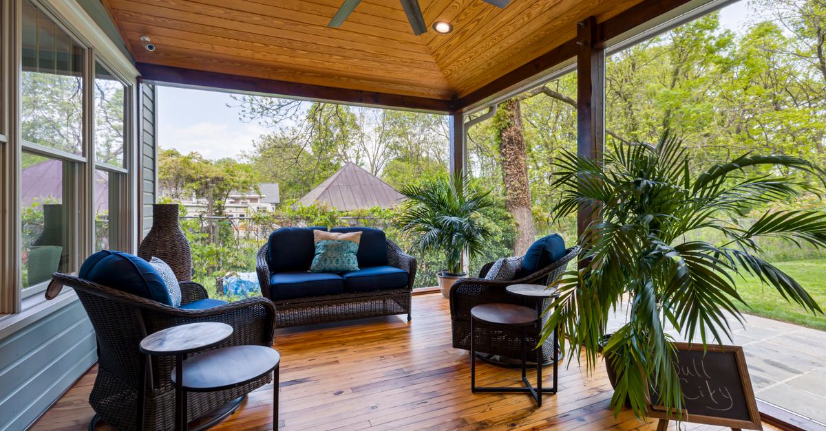 Stylish outdoor patio with cushioned seating, wooden flooring, and lush greenery.