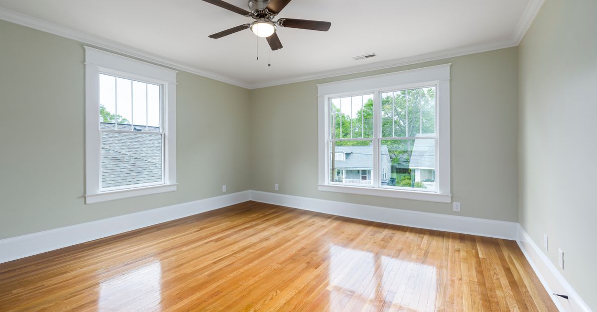 Bright empty room with wooden floors, large windows, and a ceiling fan.