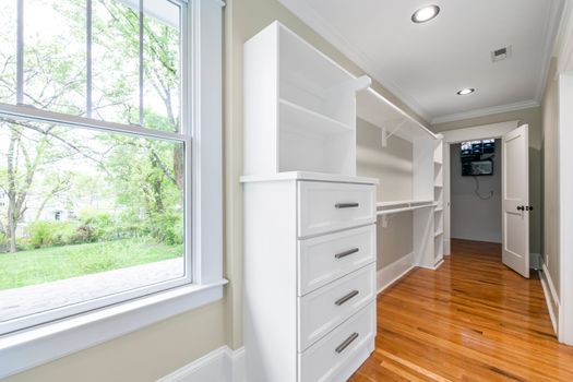 Spacious, light-filled walk-in closet featuring white shelves and drawers with hardwood floors.
