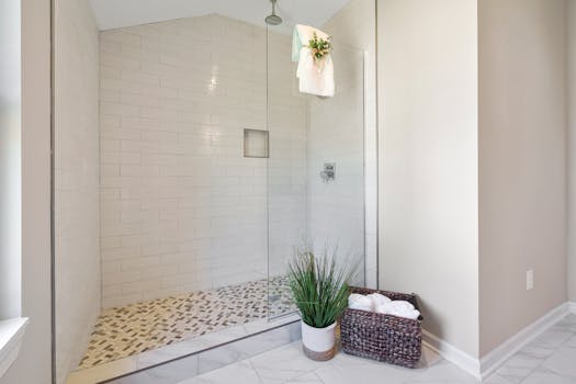 A minimalist bathroom featuring a sleek glass shower design with decorative plants and neatly arranged towels.