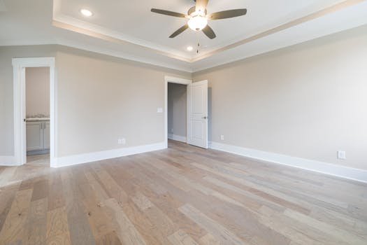 Bright empty room with wooden floors, ceiling fan, and open doors.