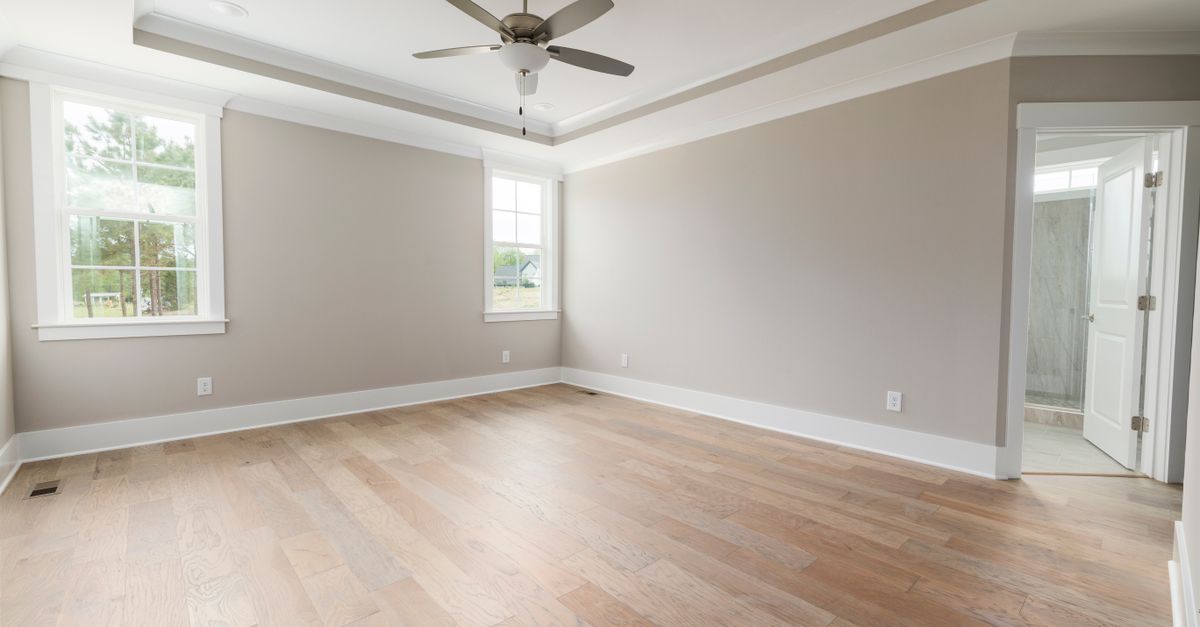 Open, modern bedroom with wooden floors and ceiling fan, ideal for staging.