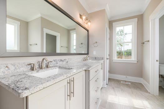 Elegant bathroom featuring a granite countertop, large mirror, and natural light.