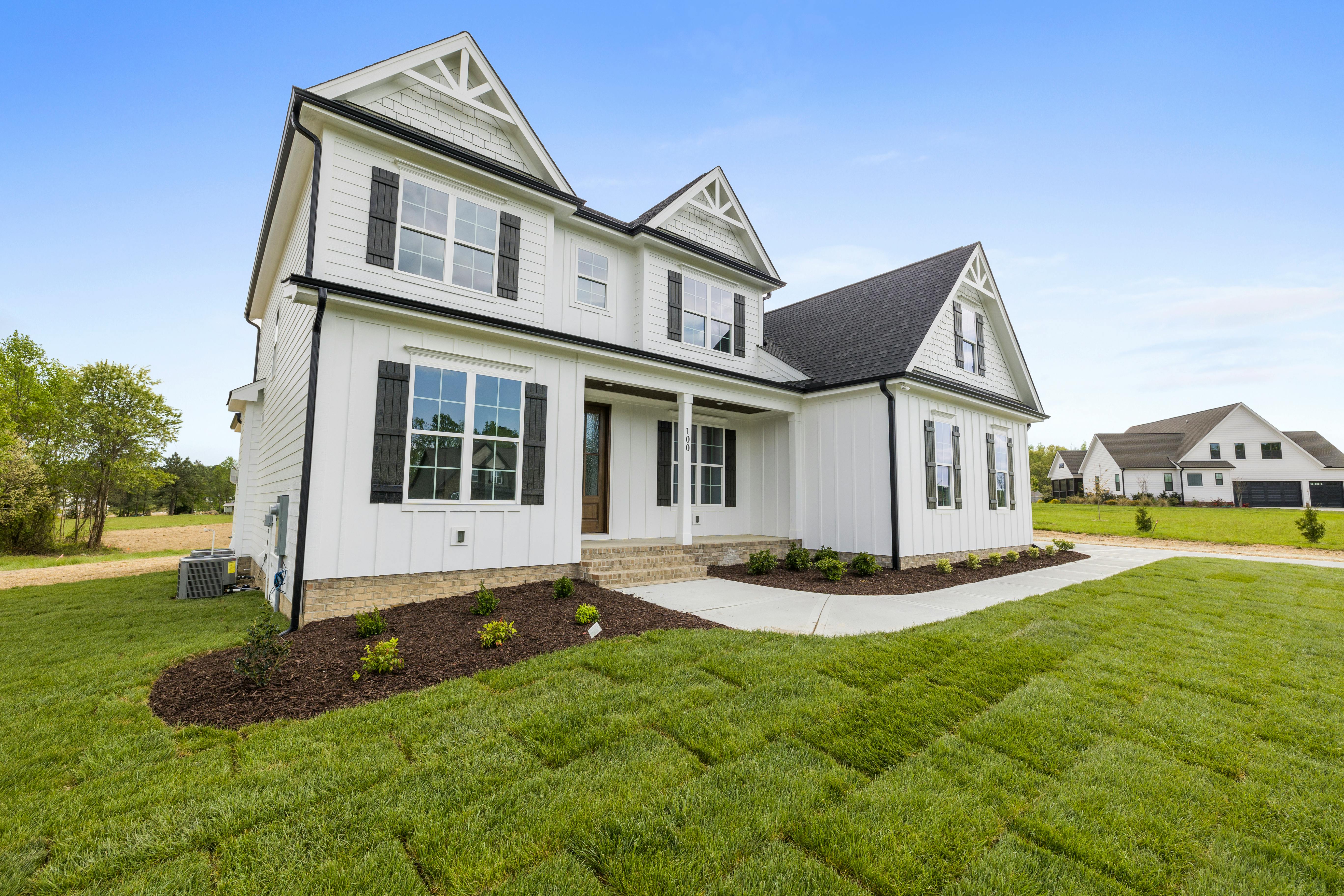 White farmhouse-style house with black shutters on a grassy lawn under a blue sky.