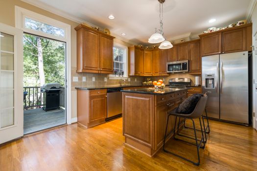 Bright modern kitchen with wooden cabinets, island, and stainless steel appliances.