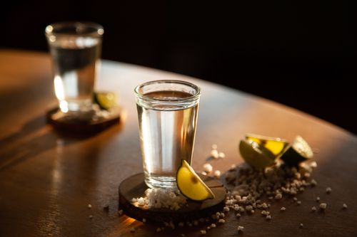 Free Close-up shot of a tequila glass with lime and salt on a warm-lit wooden table. Stock Photo