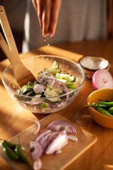 Close-up of slicing vegetables in a bowl for a fresh salad with hand seasoning.