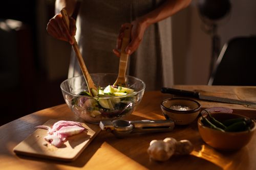 Free Hands mixing fresh cucumber and onion salad in a bowl on a wooden table. Stock Photo